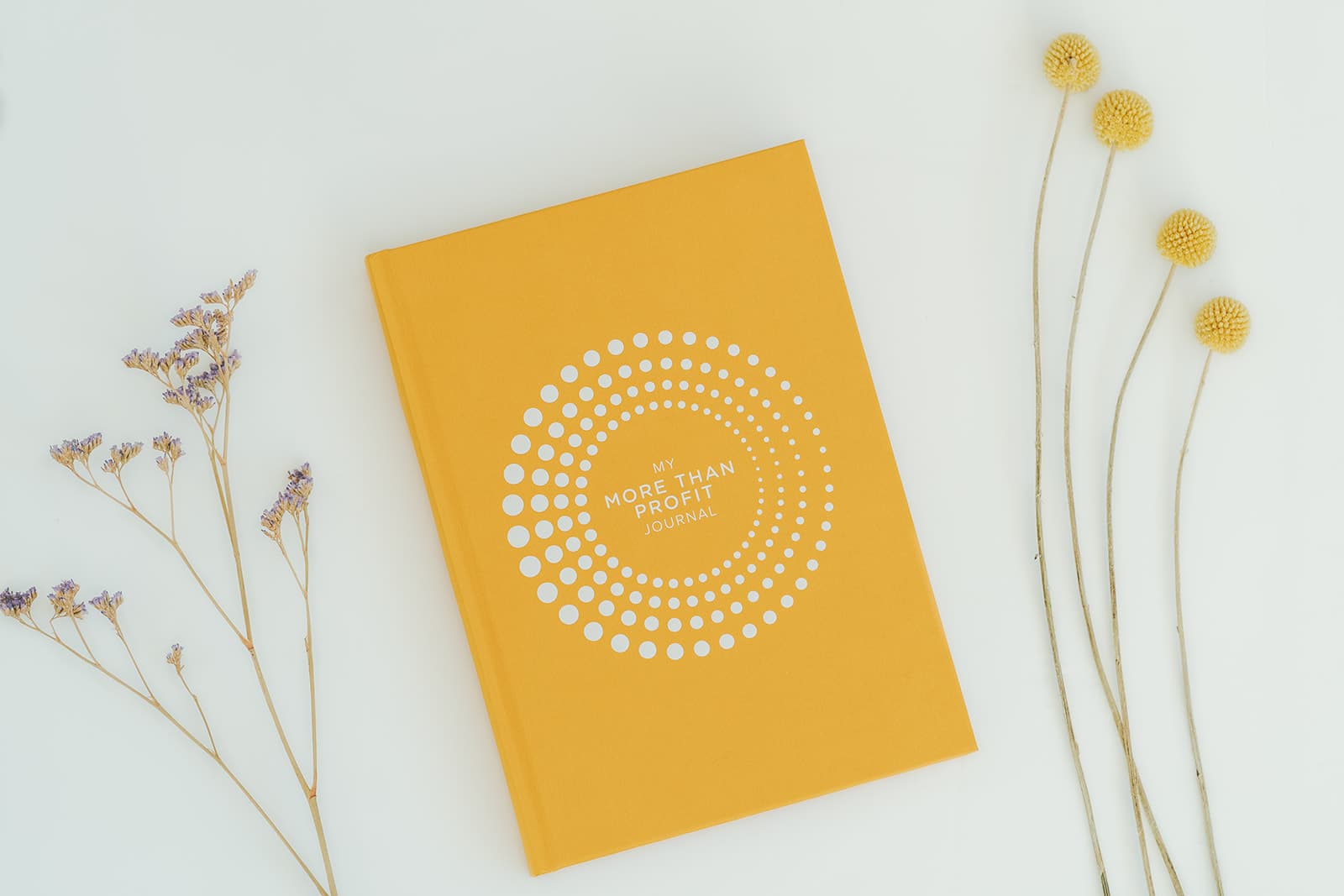 The More Than Profit Journal — a mustard-yellow hardback notebook with a white concentric dot circle on the cover.